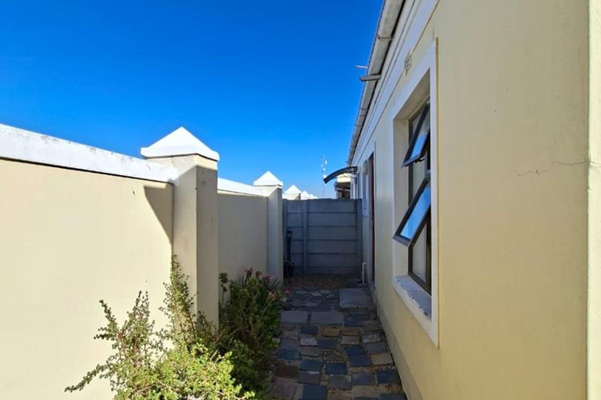 A narrow side walkway featuring stone paving, perimeter boundary walls, and access to the side of the townhouse structure.