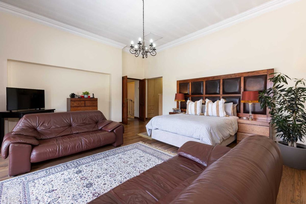 Spacious bedroom featuring high ceilings with crown molding, hardwood flooring, and a large built-in headboard wall unit.