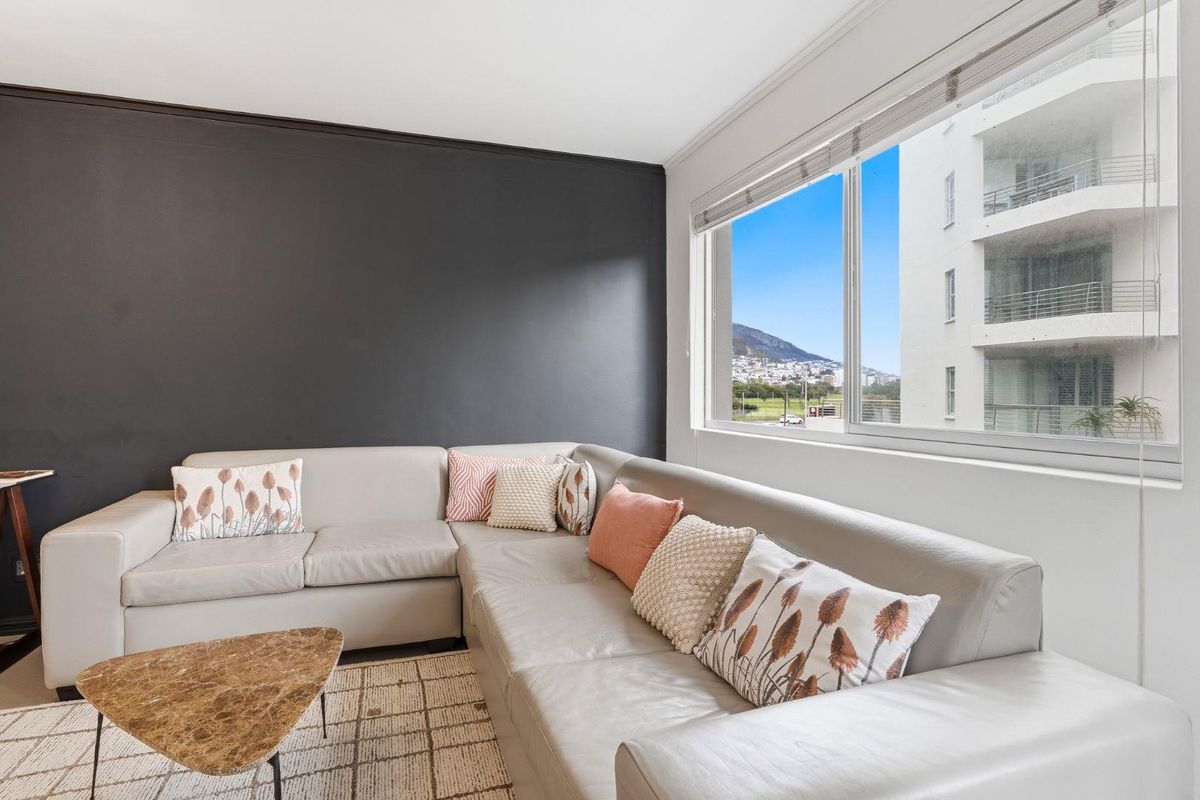 A bright living room featuring a large window with views, a dark accent wall, and neutral flooring.