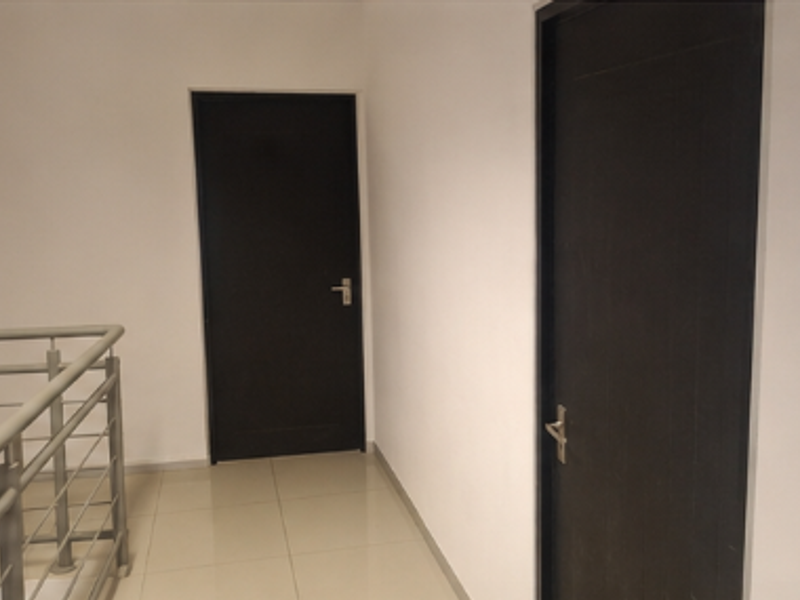 A clean, minimalist office hallway featuring tiled flooring, a modern metal balustrade, and two dark-finished internal doors.