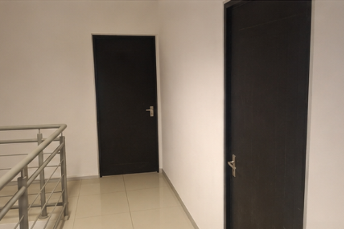 A clean, minimalist office hallway featuring tiled flooring, a modern metal balustrade, and two dark-finished internal doors.