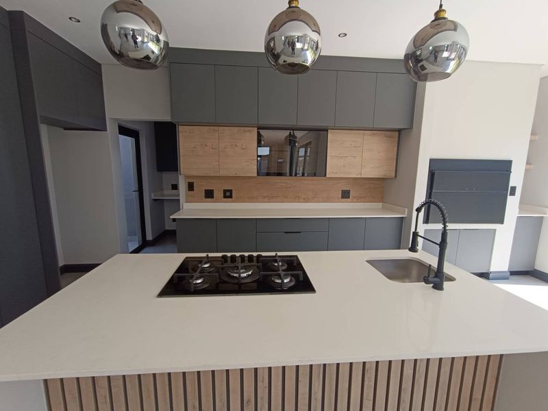 Modern kitchen featuring a central island with a gas hob, stone countertops, two-tone cabinetry, and contemporary pendant lighting.