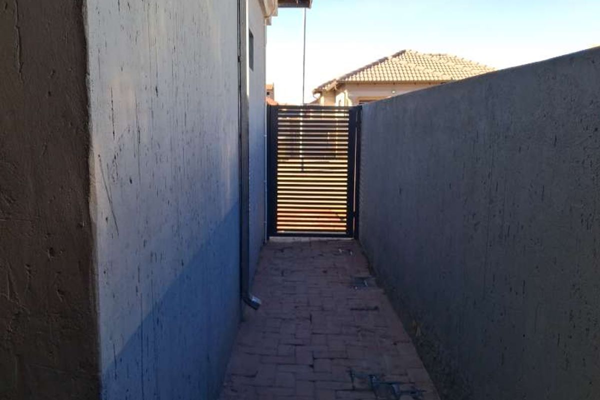 A narrow side passage featuring paved flooring, boundary walls, and a secure metal gate.
