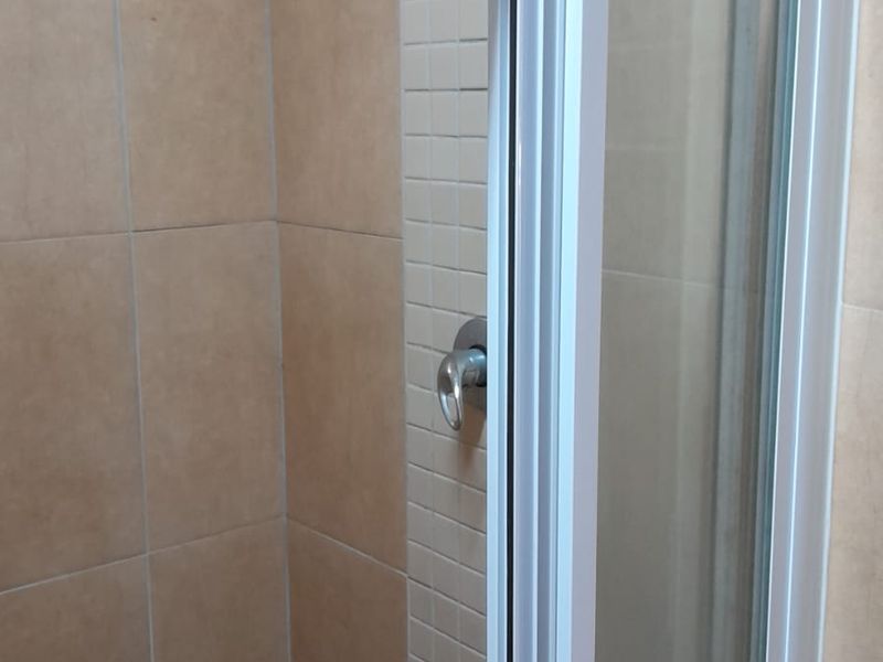 A functional shower stall featuring neutral-toned wall tiles, a glass enclosure, and a standard shower mixer tap.