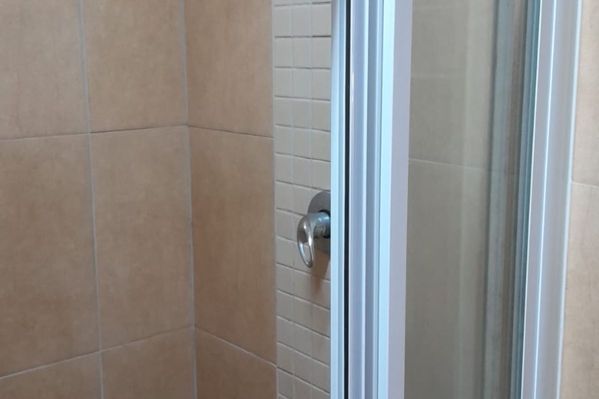 A functional shower stall featuring neutral-toned wall tiles, a glass enclosure, and a standard shower mixer tap.