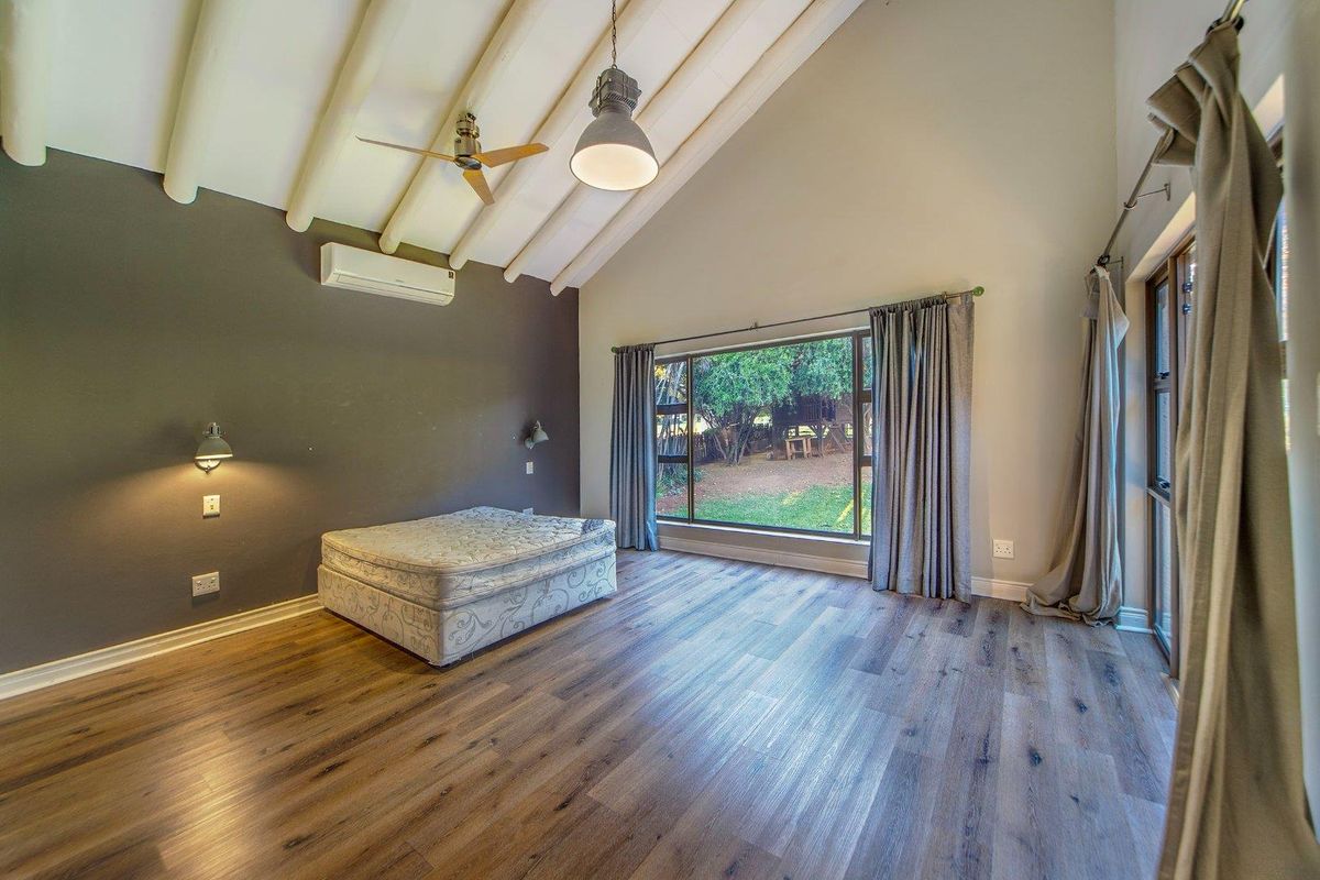 Spacious bedroom featuring high vaulted ceilings with exposed beams, wood-look flooring, split-system air conditioning, and large windows overlooking the garden.