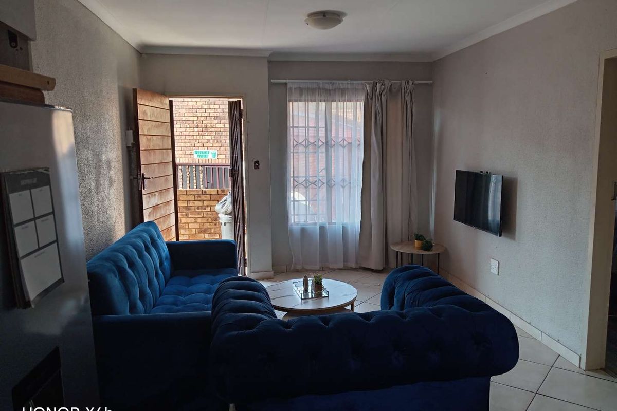A functional living room featuring tiled flooring, a security gate leading to the exterior, and a window fitted with security bars.