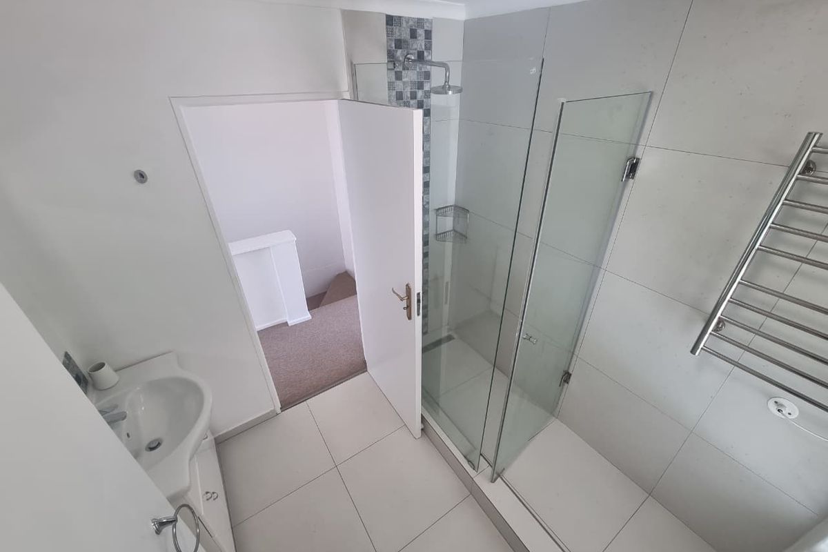 Modern bathroom featuring a walk-in shower with glass screen, vanity basin, and a heated towel rail, finished with neutral floor and wall tiles.