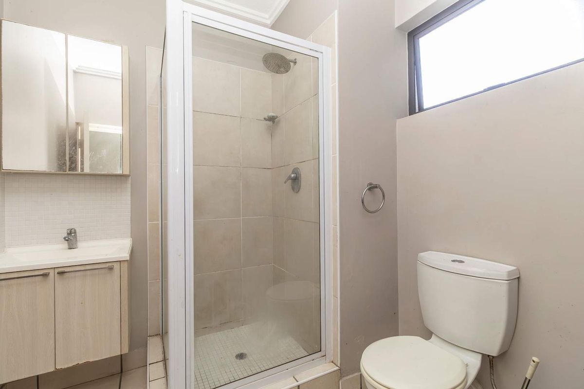 A functional bathroom featuring a glass-enclosed shower, a vanity with integrated basin, and a standard toilet.