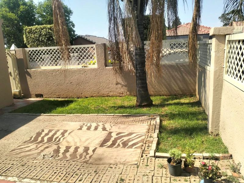 A compact private garden featuring a paved patio area, lawn, and perimeter boundary walls with decorative lattice fencing.