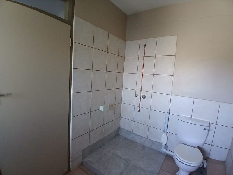 A basic bathroom featuring a toilet and exposed shower plumbing with tiled walls and flooring, requiring finishing and modernization.