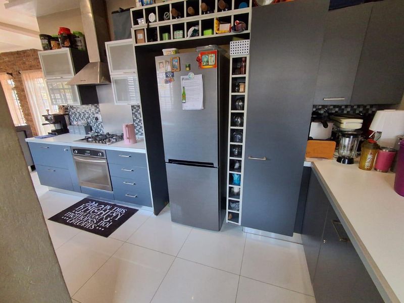 Modern kitchen featuring grey cabinetry, white countertops, a gas hob with extractor fan, and a built-in wine rack, finished with tiled flooring.