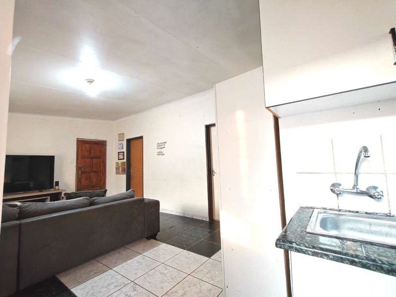 Open plan living area featuring a compact kitchen corner with sink and tiled flooring, connecting to the main living space.