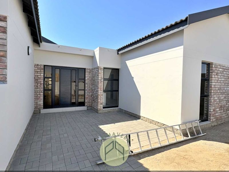 A modern rear exterior view featuring a paved patio area, brick and plaster facade, and contemporary aluminium-framed windows and doors.