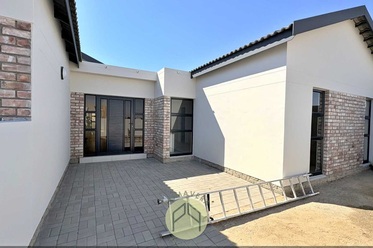 A modern rear exterior view featuring a paved patio area, brick and plaster facade, and contemporary aluminium-framed windows and doors.