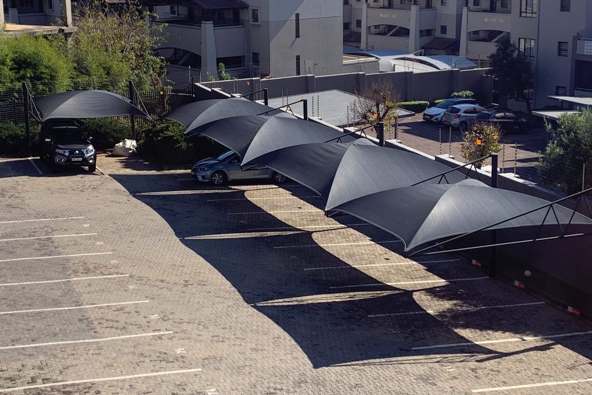 An elevated view of a paved parking area featuring multiple shade-cloth carports for vehicle protection.