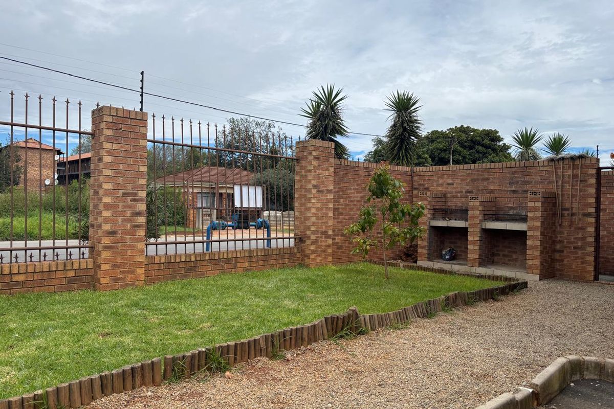 A private outdoor area featuring a built-in brick braai, enclosed by a secure brick and metal perimeter fence with a small grassed garden.
