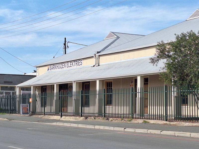 Front exterior view of an industrial property featuring a corrugated metal roof, covered veranda, and secure perimeter fencing.