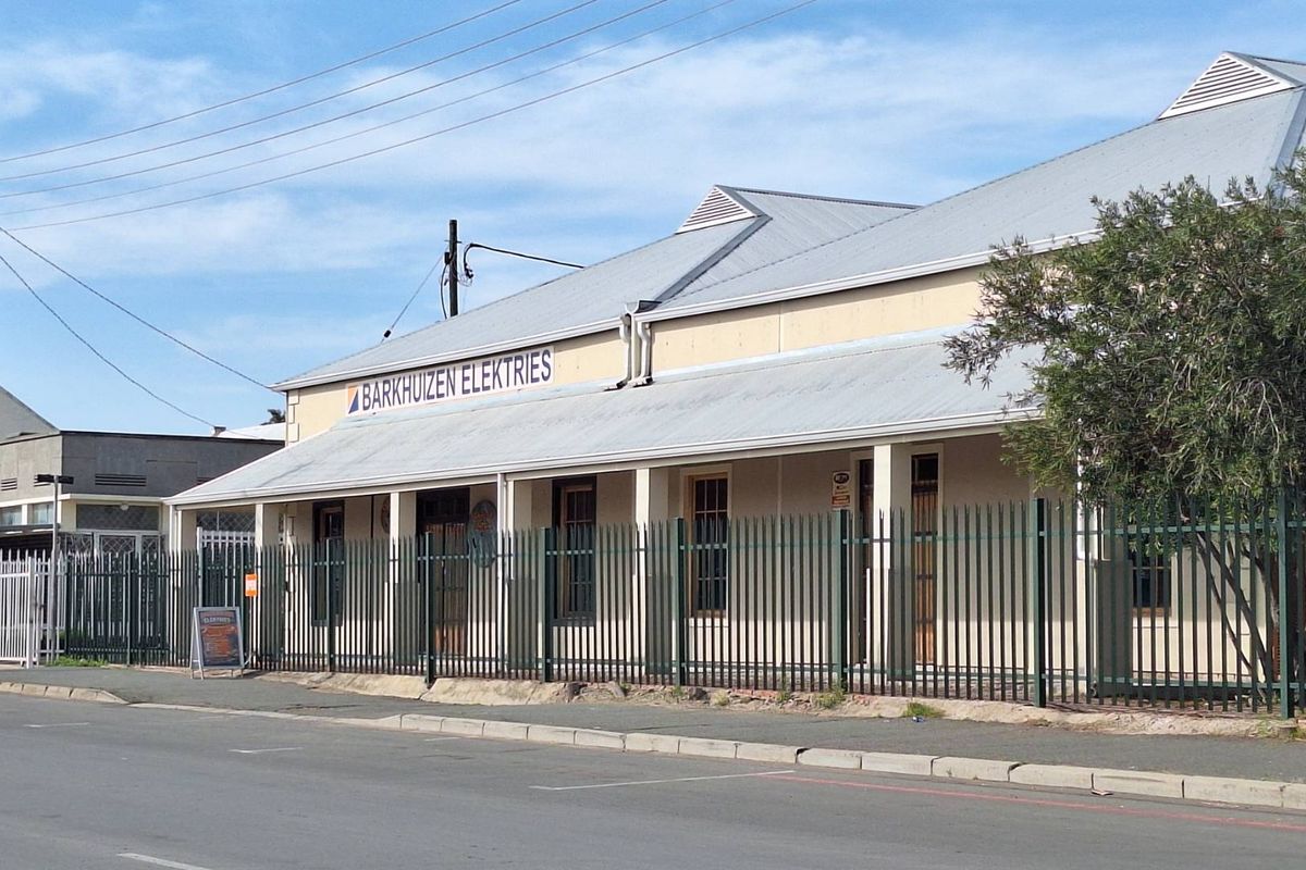Front exterior view of an industrial property featuring a corrugated metal roof, covered veranda, and secure perimeter fencing.