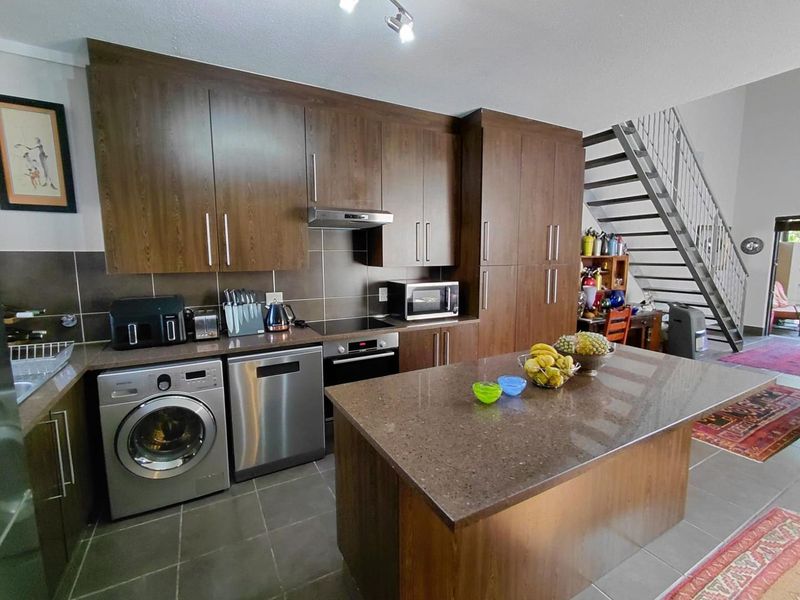 Open-plan kitchen featuring dark wood cabinetry, stone countertops, a central island, and integrated appliances, with an adjacent staircase leading to the upper level.