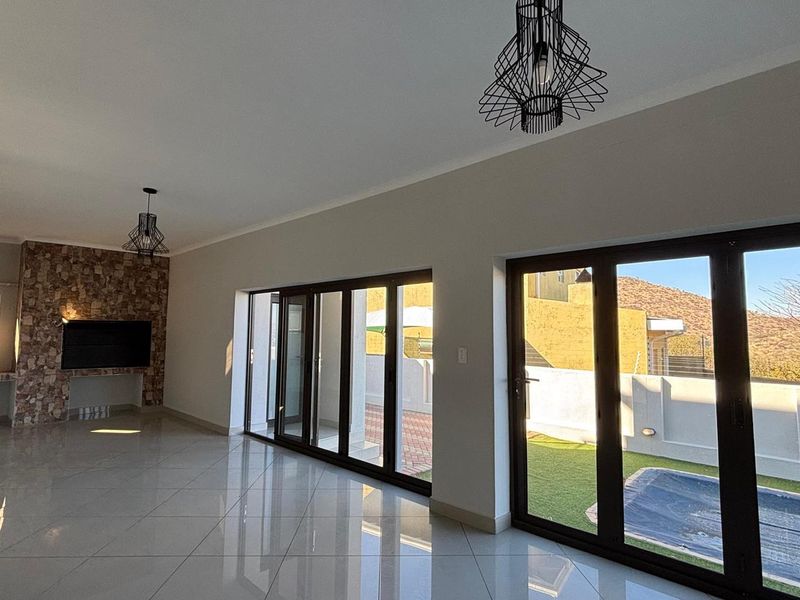 Spacious living area featuring large aluminium stacker doors opening to the patio, polished tiled floors, and a decorative stone-clad feature wall.