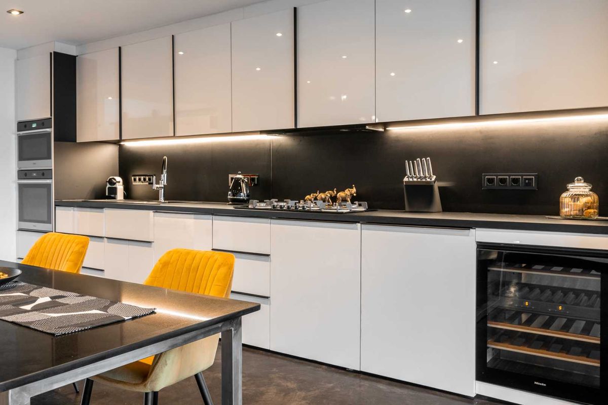 Modern kitchen featuring high-gloss white cabinetry, integrated appliances, a gas hob, and sleek black stone countertops with ambient under-cabinet lighting.