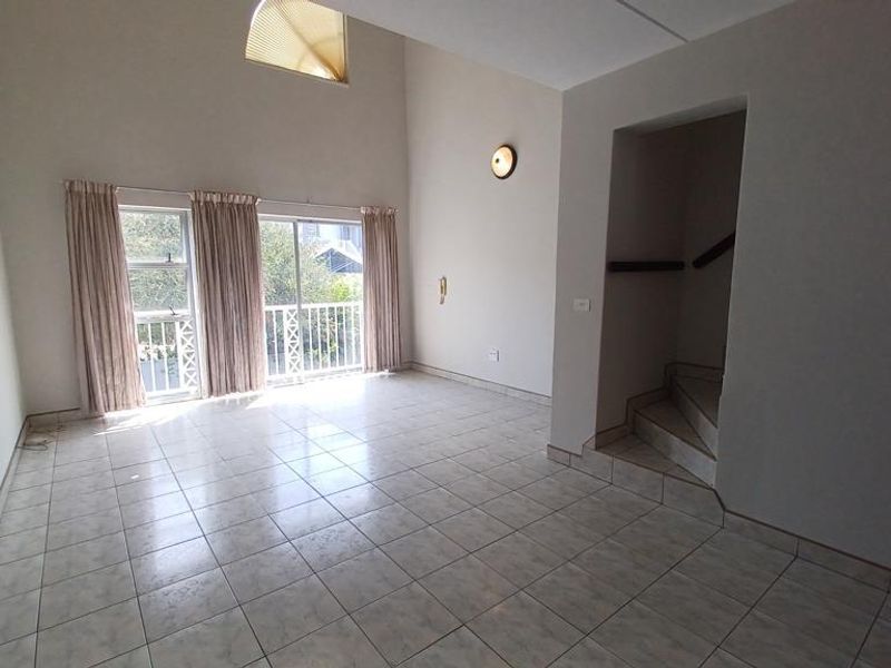 Spacious, light-filled living area featuring high vaulted ceilings, tiled flooring, and sliding glass doors leading to a balcony, with an adjacent staircase.