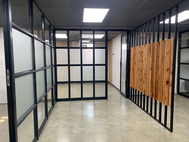 Modern office space featuring polished concrete floors, black metal-framed glass partitions, and a decorative vertical timber slat feature wall.