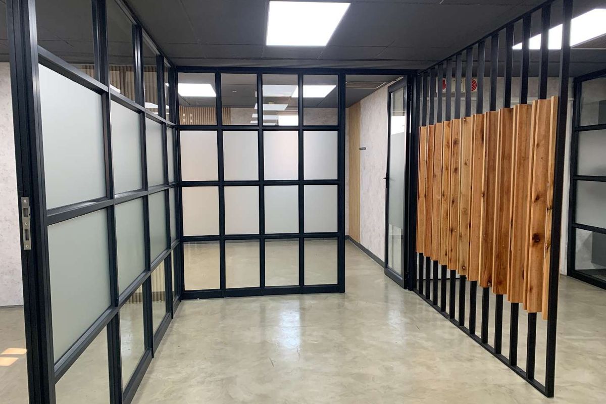 Modern office space featuring polished concrete floors, black metal-framed glass partitions, and a decorative vertical timber slat feature wall.