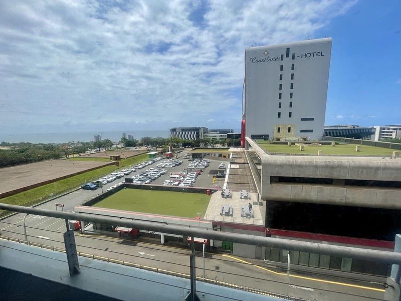 Elevated urban view overlooking a parking area, commercial buildings, and the distant coastline.