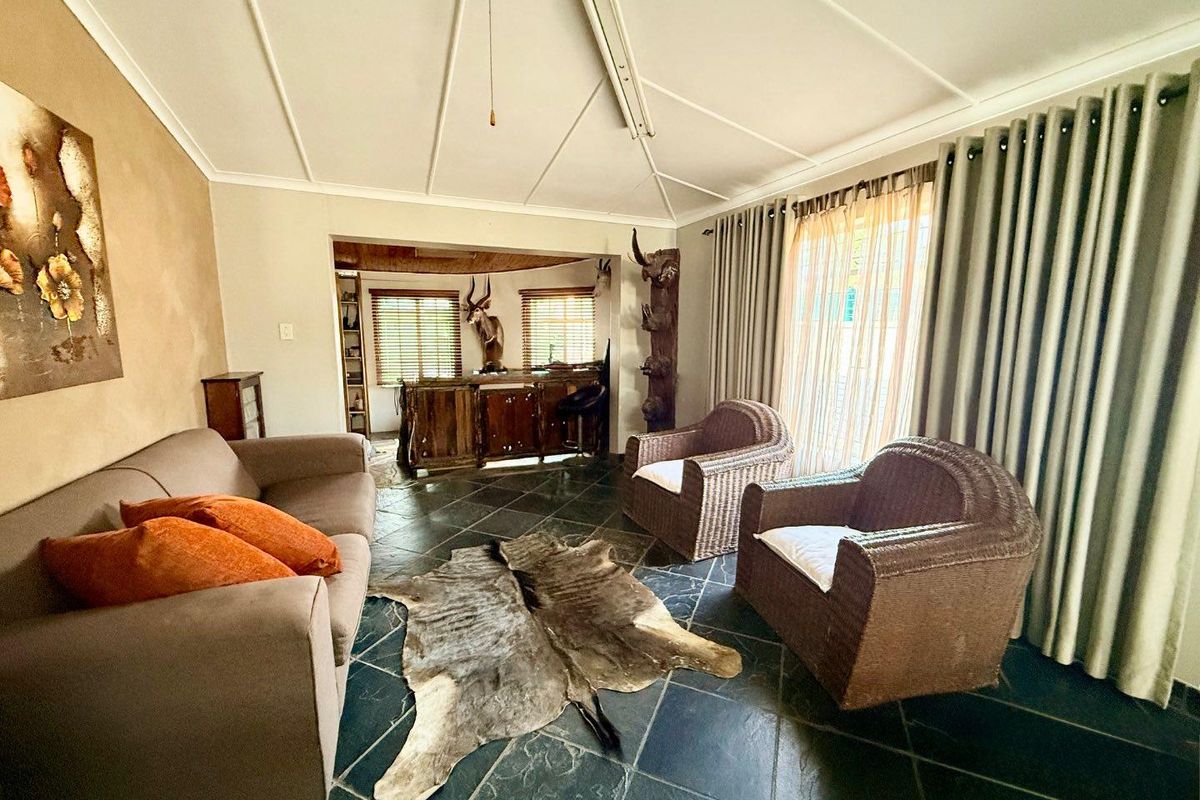 A spacious living area featuring dark slate flooring, a built-in bar area, and large windows with curtains.