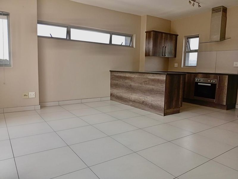 Modern open-plan kitchen featuring wood-finish cabinetry, a central island, built-in oven, extractor fan, and neutral tiled flooring throughout the living space.