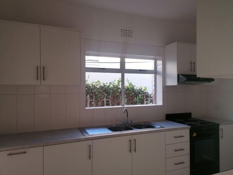 A functional kitchen featuring white cabinetry, a double-basin stainless steel sink, tiled splashbacks, and a built-in oven with an extractor fan.