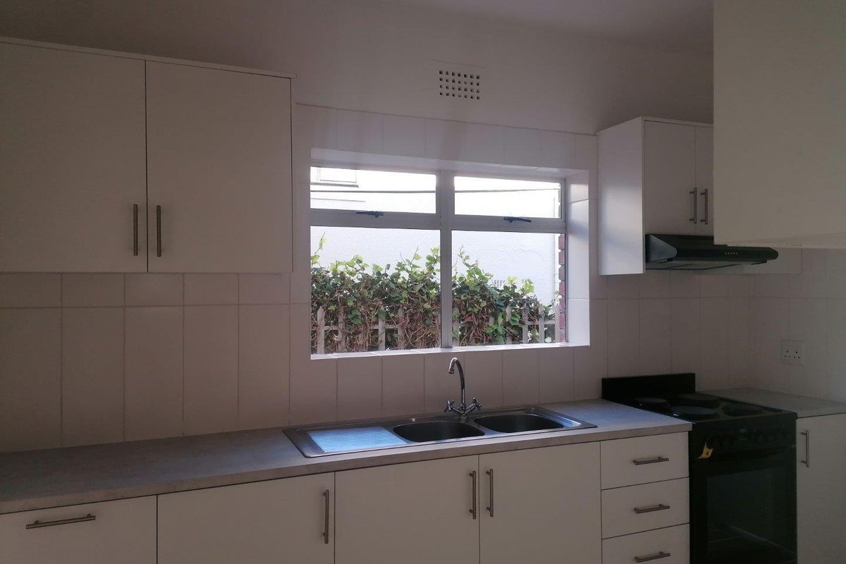 A functional kitchen featuring white cabinetry, a double-basin stainless steel sink, tiled splashbacks, and a built-in oven with an extractor fan.