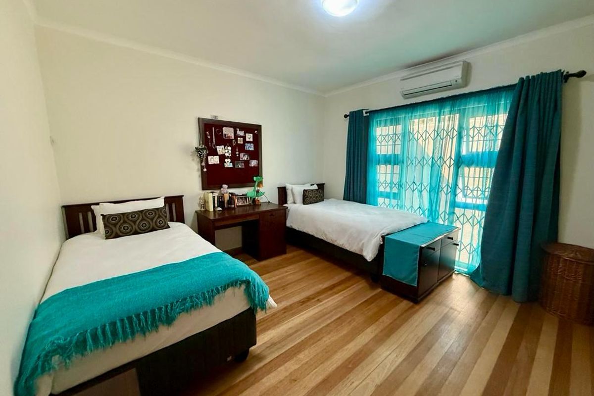 A spacious bedroom featuring polished wooden flooring, a wall-mounted air conditioning unit, and large windows with security bars.