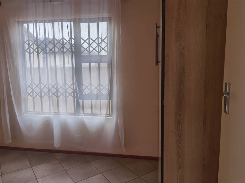 A bright bedroom featuring tiled flooring, a built-in wardrobe, and a window fitted with a security gate.