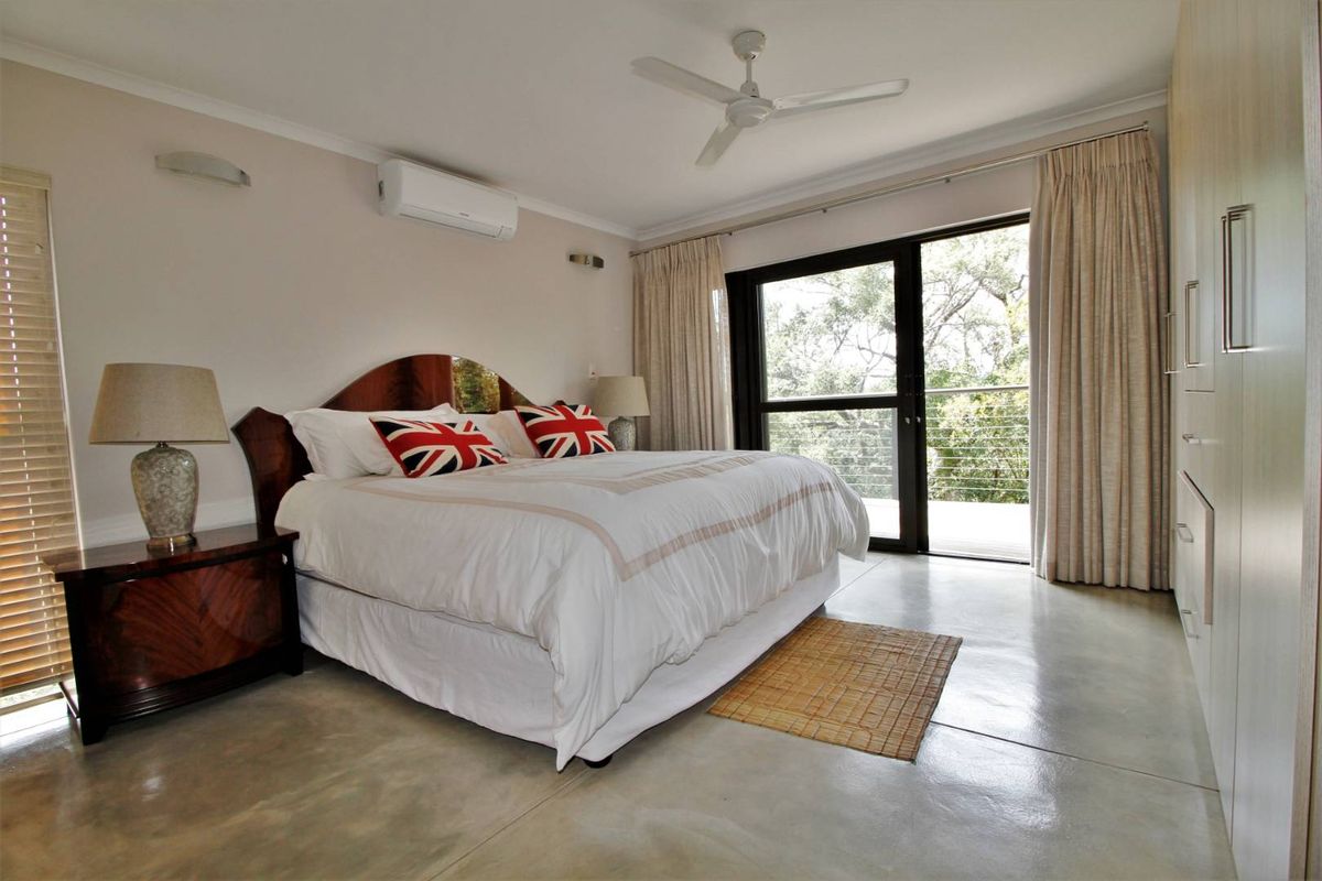 Spacious bedroom featuring polished concrete flooring, built-in cabinetry, a ceiling fan, wall-mounted air conditioning unit, and sliding glass doors opening to a balcony.