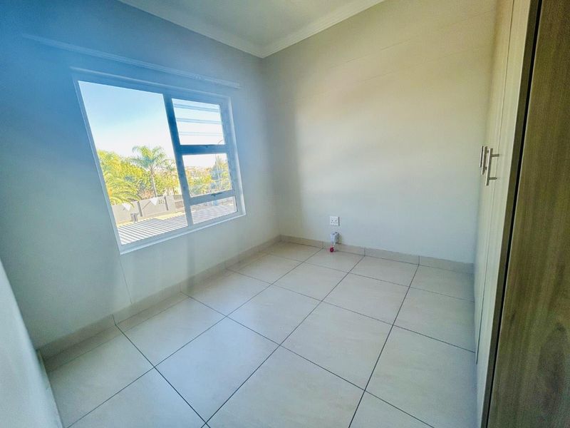 A bright, empty bedroom featuring neutral tiled flooring, built-in cupboards, and a large window providing natural light.