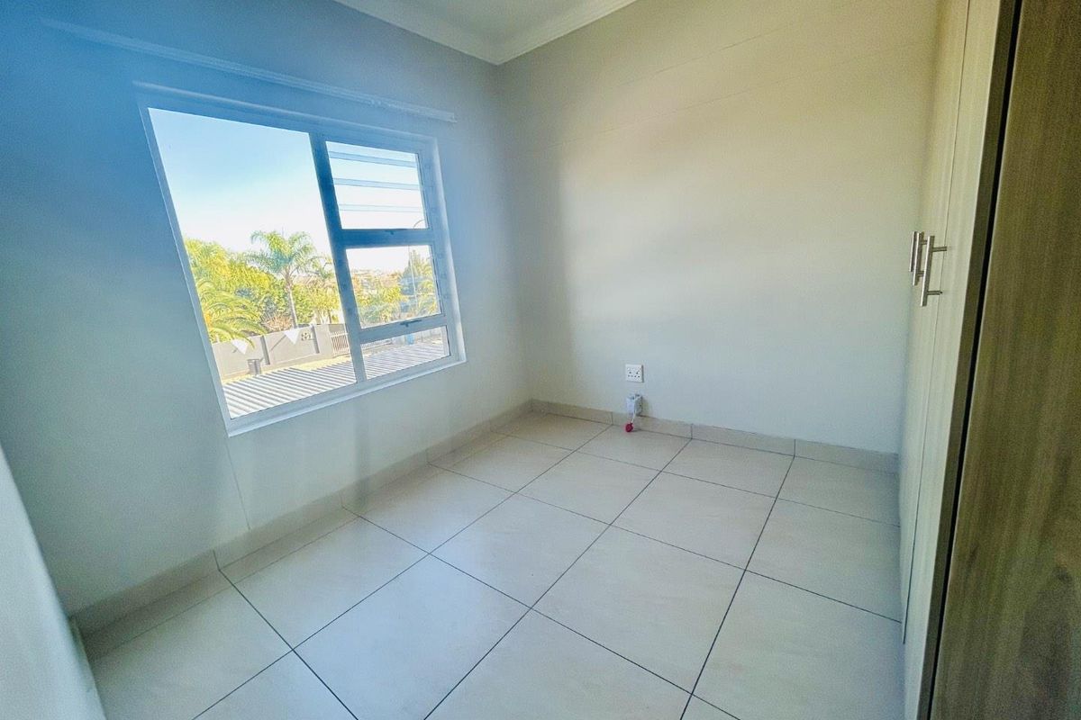 A bright, empty bedroom featuring neutral tiled flooring, built-in cupboards, and a large window providing natural light.