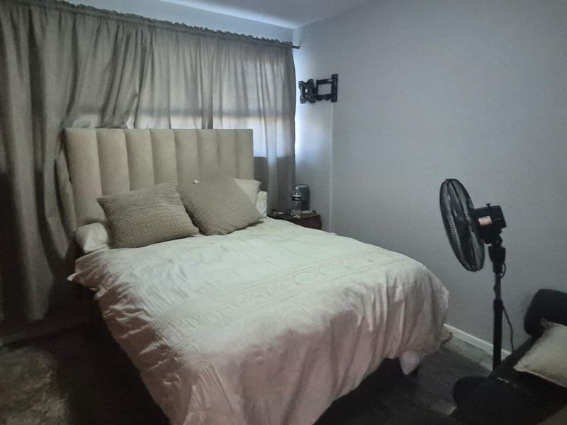 A standard bedroom featuring a neutral color palette, curtained window, and wall-mounted television bracket.