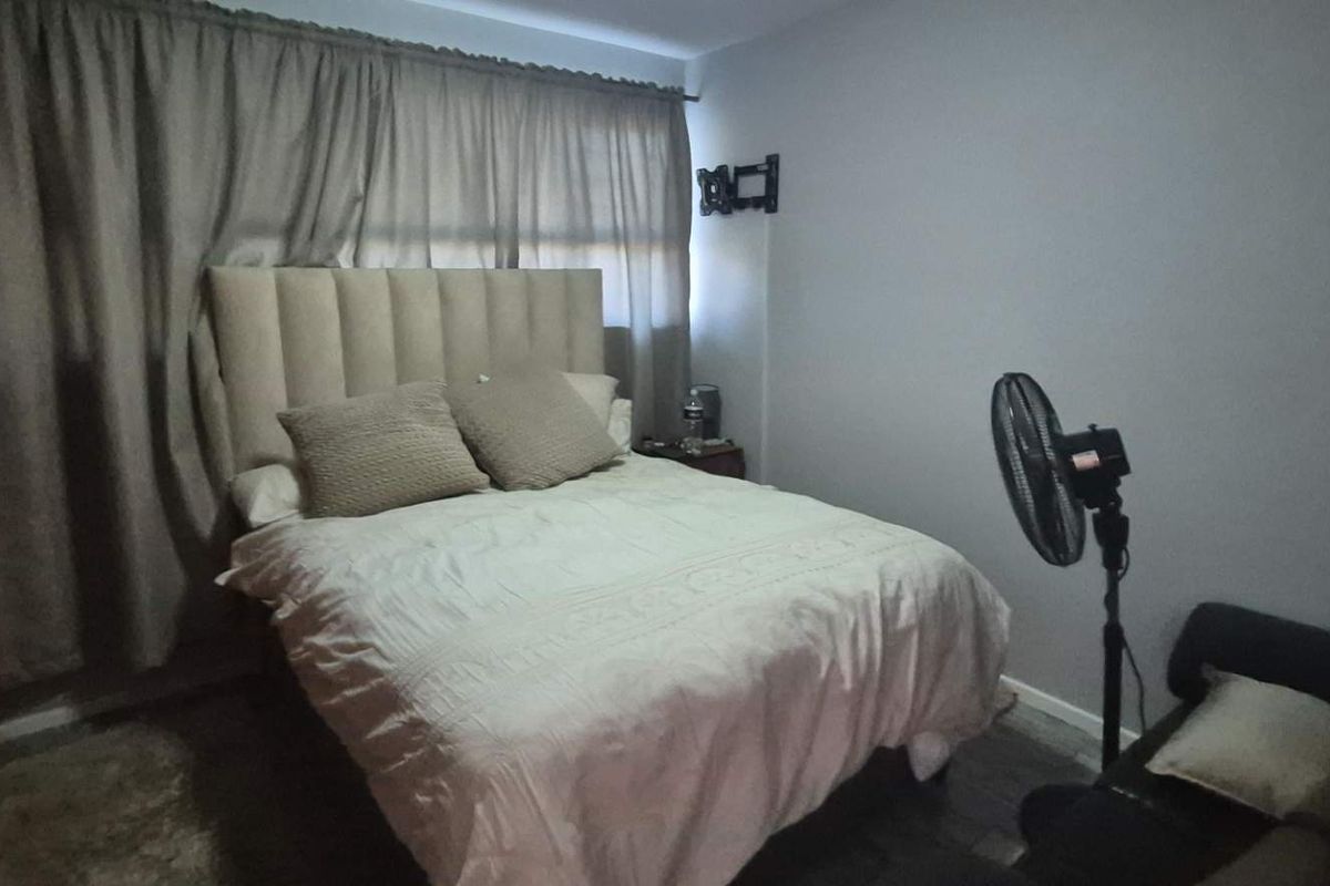 A standard bedroom featuring a neutral color palette, curtained window, and wall-mounted television bracket.