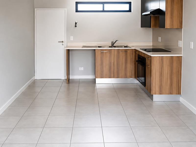 Modern, empty kitchen featuring wood-finish cabinetry, stone-look countertops, integrated electric hob and oven, and neutral tiled flooring.