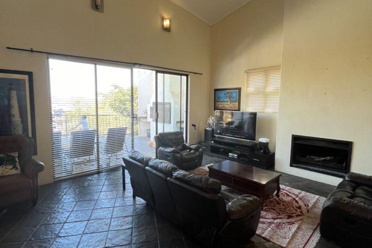Spacious living room featuring high vaulted ceilings, dark slate tile flooring, and a built-in fireplace, with large sliding doors leading to an outdoor patio.