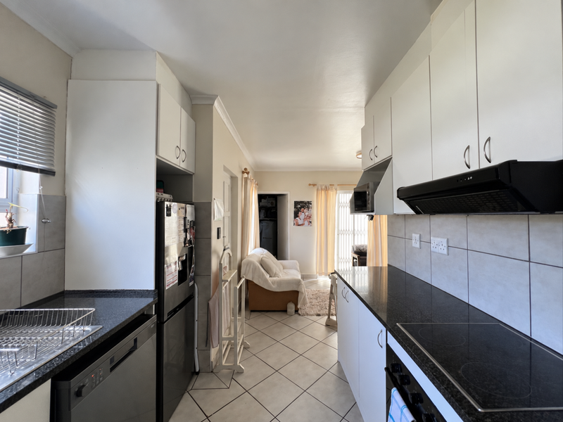 Open-plan kitchen featuring granite countertops, built-in cabinetry, and an electric hob, flowing into a living area with tiled flooring throughout.