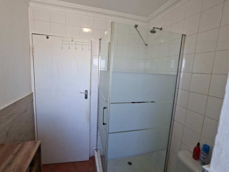 A functional bathroom featuring a glass shower enclosure, ceramic wall and floor tiling, and standard sanitary ware.