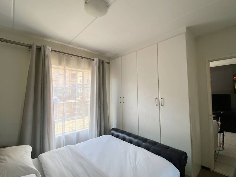 A functional bedroom featuring built-in cupboards and a window with natural light, providing a clean and practical living space.
