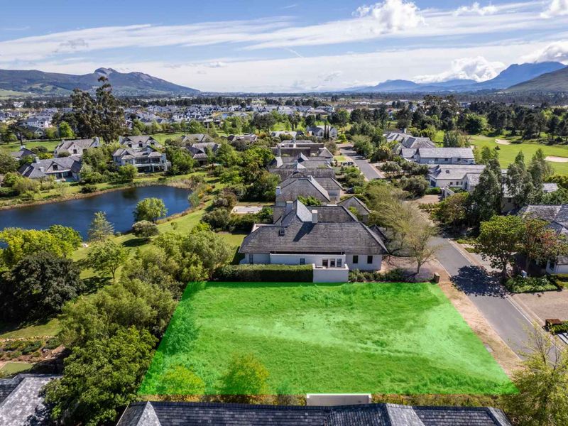 An aerial view of a vacant residential plot situated within a well-established estate, featuring surrounding greenery and proximity to a scenic lake.