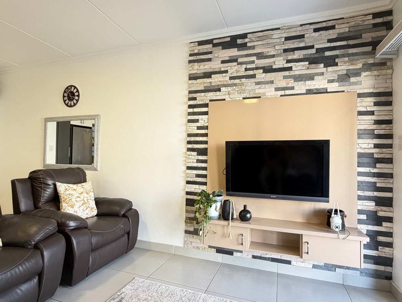 A well-maintained living room featuring a modern stacked stone accent wall with a built-in media console and neutral tiled flooring.