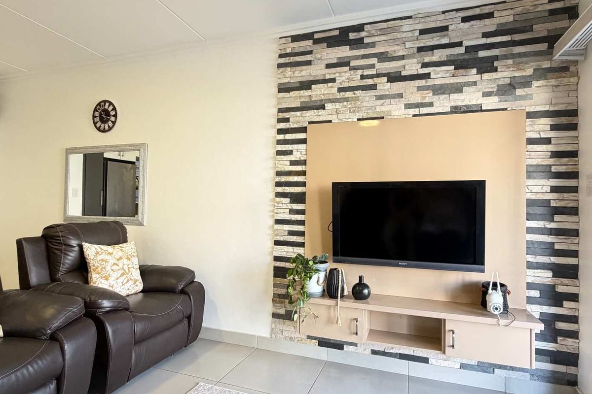 A well-maintained living room featuring a modern stacked stone accent wall with a built-in media console and neutral tiled flooring.