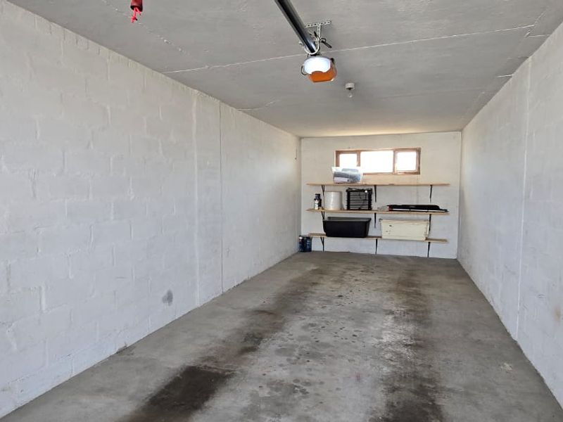 A spacious, empty single-car garage featuring painted blockwork walls, a concrete floor, and built-in wall shelving for storage.